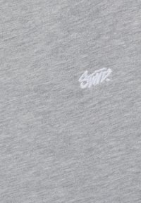 Tissu gris clair avec un petit texte brodé en blanc "SMTH." centré sur la surface.