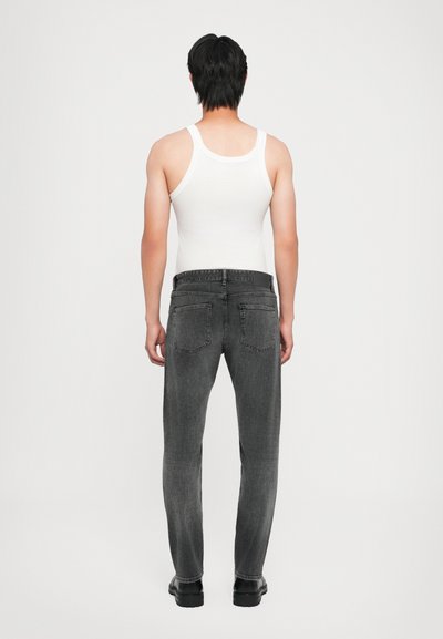 Jean en denim gris avec une coupe droite, comportant deux poches arrière, porté avec un débardeur blanc. La texture semble douce avec un léger dégradé.