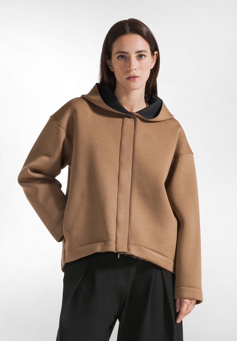 Bruine hooded sweatshirt met een zwarte voering, oversized ontwerp, geribde manchetten en een voorkant met rits. Zachte textuur, casual pasvorm.