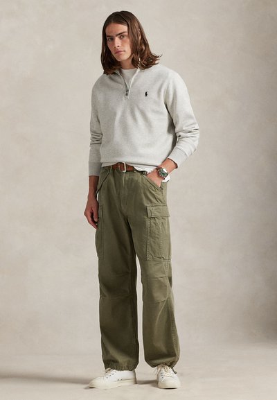 Sweatshirt cinzento claro com fecho de correr e logótipo pequeno, combinado com calças cargo largas de tom azeitona com bolsos. O look completa-se com ténis brancos.