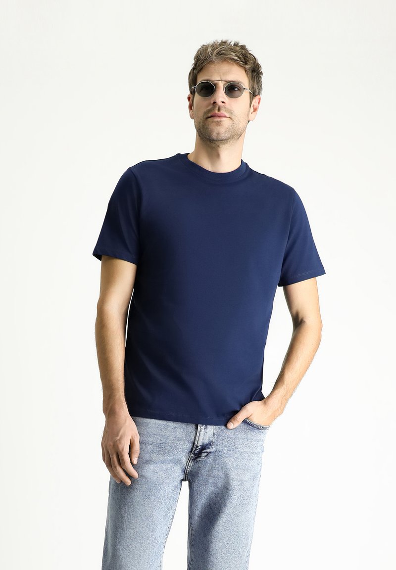 Granatowa koszulka z krótkim rękawem z okrągłym dekoltem, wykonana z gładkiego materiału. Połączona z jasnoniebieskimi dżinsami.