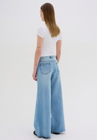 Light blue wide-leg jeans with a high waist, featuring a classic five-pocket design and frayed hem, paired with a fitted white t-shirt.