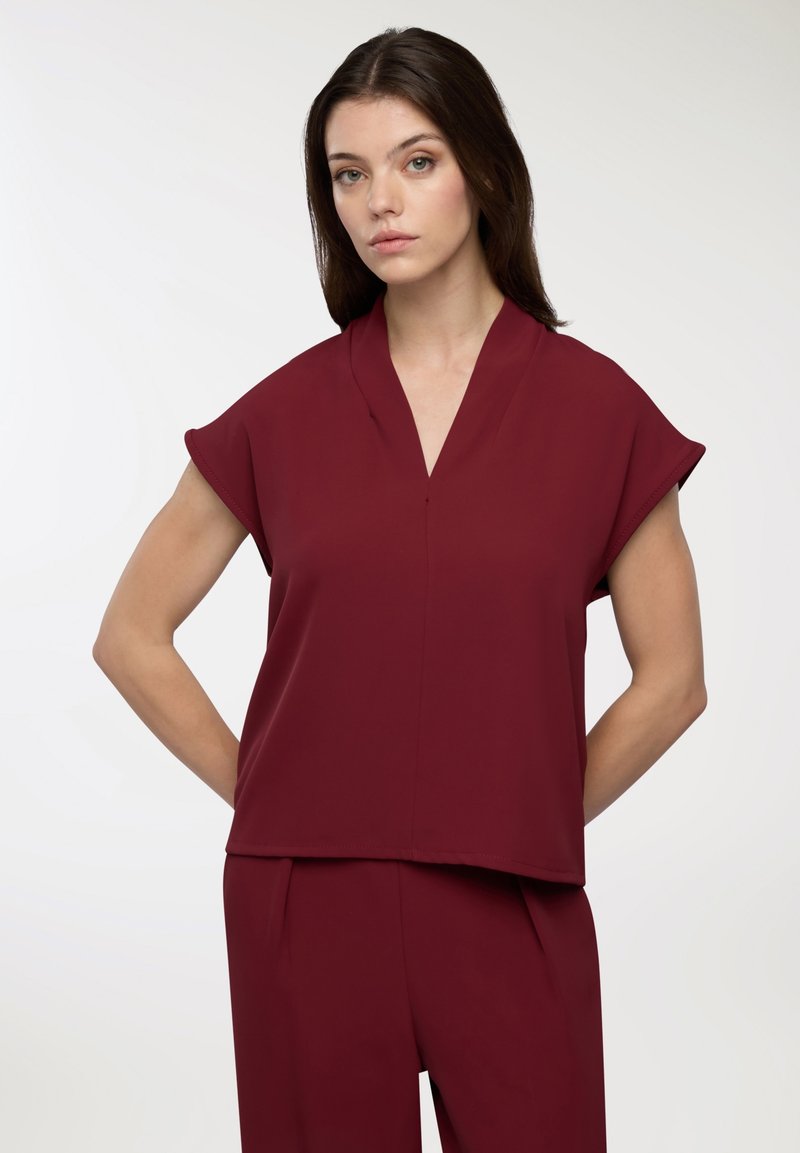 Top corto bordeaux con scollatura a V, realizzato in tessuto morbido, caratterizzato da una vestibilità comoda e un orlo dritto.