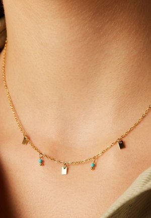 Goldkette mit kleinen, flachen geometrischen Anhängern und Türkisperlen, die ein zartes, geschichtetes Design erzeugen.