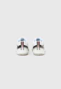 Λευκά αθλητικά παπούτσια με βαθμιαία μετάβαση από γκρι σε μαύρο στη φτέρνα, κόκκινες και λευκές ριγέ λεπτομέρειες και απαλό γαλάζιο εσωτερικό επένδυση.