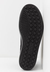 Black rubber shoe sole with a textured, dotted pattern for grip. Features a smooth edge, minimal design, and embossed brand logo.