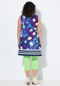 Bezrękawnik z wyrazistym abstrakcyjnym wzorem w purpurowych i niebieskich odcieniach, granatowe paski na dole. Połączony z zielonymi legginsami do kolan i białymi botkami.