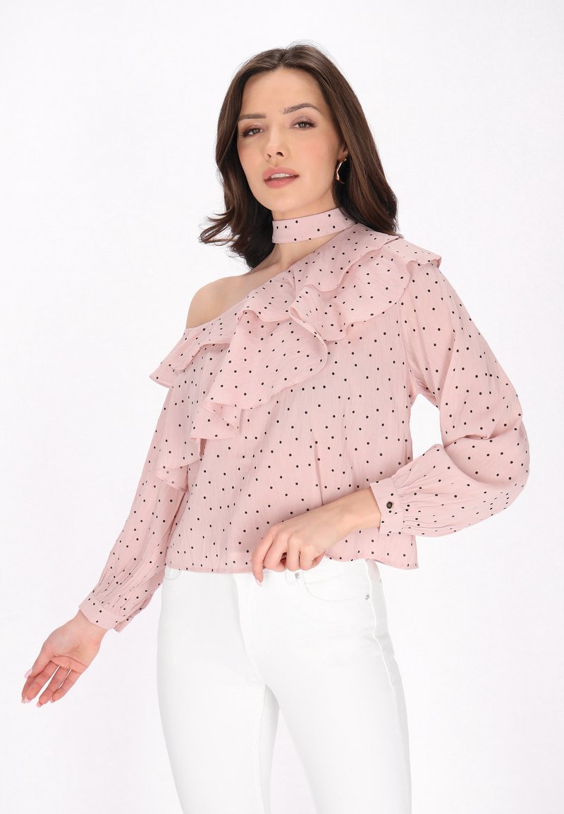 Helles pinkes Blusenshirt mit schwarzen Punkten, off-the-shoulder-Design, rüschigem Vorderteil, langen Ärmeln und hohem Kragen. Mit einem feinen Glanz akzentuiert.