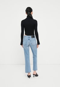 Maglione a collo alto nero a coste, aderente in vita, abbinato a jeans a gamba dritta blu chiaro, con etichetta nera alla vita.