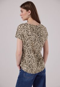 Beige Oberteil mit einem schwarzen Leopardenmuster, kurzen Ärmeln und einem runden Ausschnitt. Der Stoff sieht glatt aus und hat eine lockere Passform.