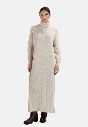 Longo vestito lavorato a maglia color crema con collo alto, texture a coste e maniche lunghe, abbinato a stivaletti marroni alla caviglia.