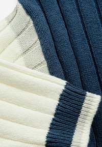 Pletená látka v námorníckej modrej a krémovej farbe, s rebrovou textúrou a striedajúcimi sa pruhmi. Mäkká, hrubá priadza vytvára útulný vzhľad.