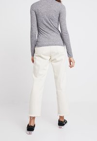 Graues, geripptes Langarmoberteil kombiniert mit cremefarbenen, cropped Jeans mit fransigen Säumen und schwarzen Sneakers, von hinten betrachtet.
