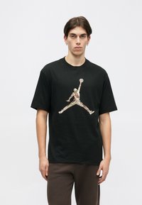 Schwarzes T-Shirt aus Baumwolle mit kurzen Ärmeln, auf dessen Vorderseite ein großes, mehrfarbiges Air Jordan-Logo prangt. Einfaches Rundhals-Design.