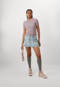 Lila, kabelstickad kortärmad tröja i kombination med en ljusblå denim mini-kjol, grå knästrumpor och blekrosa hög-top sneakers.