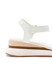 Sandalias blancas con un diseño plano y una suela gruesa y apilada. La parte superior presenta una tira texturizada y un acabado suave y mate.