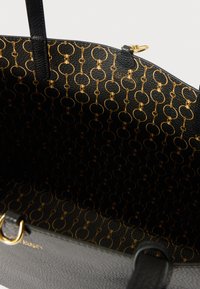 Čierna kožená kabelka typu tote s vnútorným podšívkou so zlatým reťazovým vzorom a zlatým zipsom na hornej hrane.