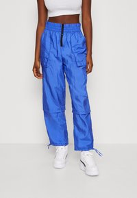 Pantalones cargo de ripstop azules con cintura elástica, dos bolsillos delanteros y puños ajustables. Llevados con zapatillas de plataforma blancas.