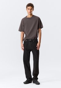 Camiseta gris de gran tamaño combinada con jeans negros de pierna recta. La camiseta tiene un escote amplio; la tela parece suave. Anillos notables en los dedos.