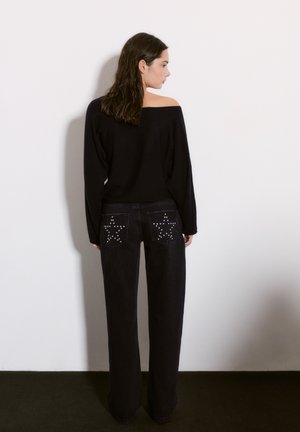 Čierny sveter bez ramienok skombinovaný s čiernymi džínsami s vysokým pásom, ktoré majú hviezdne vzory a ozdoby na zadných vreckách.