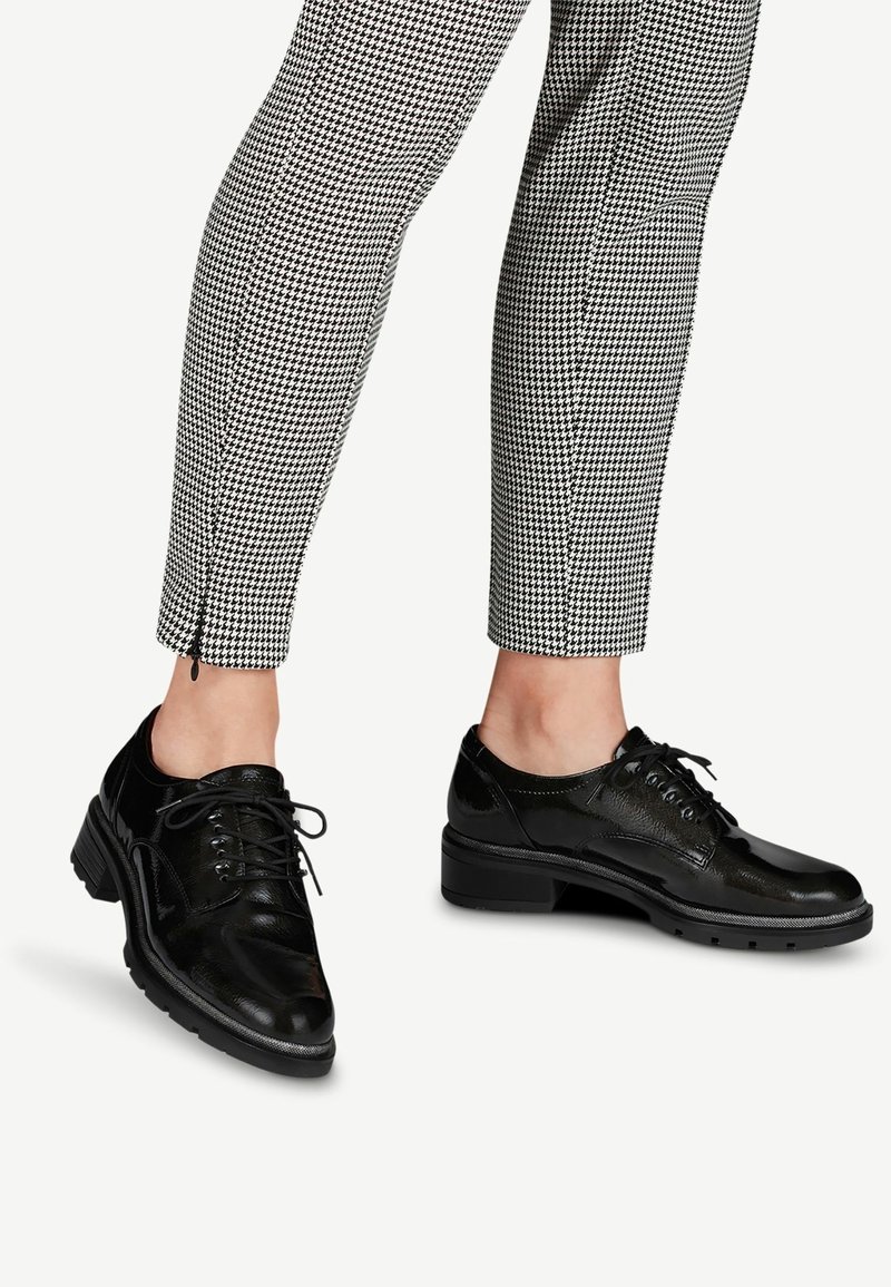 Chaussures à lacets en cuir noir poli portées avec un pantalon court pied-de-poule noir et blanc avec fermetures éclair à la cheville.