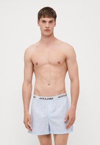 Boxers rayés bleu clair avec une ceinture élastique noire portant "JACK & JONES" imprimé en blanc. Tissu lisse et coupe ample.
