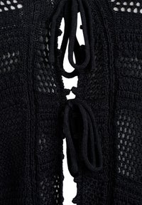 Svart stickad cardigan med en strukturerad öppen väv och knytning i halsen, med en blandning av mönster genom tyget.