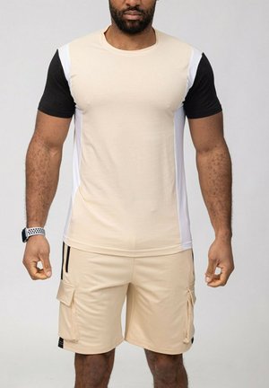 Chemise beige à manches courtes avec des accents noir et blanc, associée à un short cargo beige avec des poches latérales et une bordure noire. Texture de tissu douce.