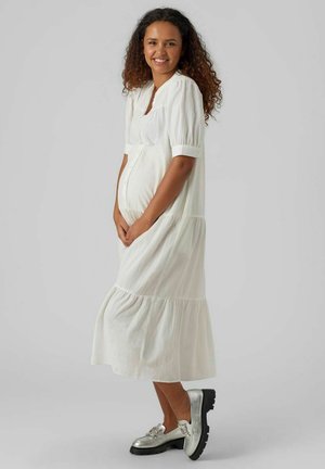 Robe midi blanche avec de courtes manches bouffantes et un design à étages, dotée d'un col rond et d'une fermeture à boutons. Associée à des chaussures argentées.