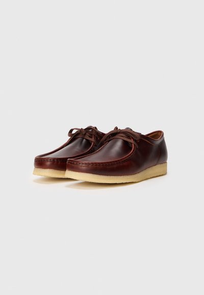 Zapatos de cuero marrón con un acabado suave, punta redonda, diseño de cordones y suela de goma beige. Presenta costuras detalladas a lo largo de los bordes.