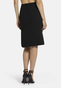 Zwarte kokerrok met een rechte silhouet, achteraan met rits en naaddetails. Gepaard met zwarte hoge hakken sandalen.