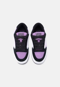 Ζευγάρι αθλητικών παπουτσιών Vans σε μαύρο, μωβ και λευκό χρώμα με μαύρα κορδόνια, από πάνω σε απλό ανοιχτό γκρι φόντο.