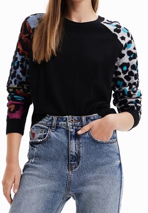 Sort sweater med lange, farverige mønstrede ærmer, der har leopard- og blomsterdesigns; stylet med højtaljede blå jeans.