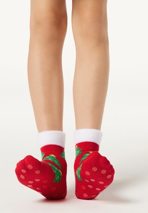 Red socks with white cuffs, featuring a green leaf pattern and dotted non-slip grips on the soles. Textured knit material.