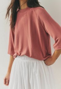 Pull rose texturé avec un col rond et des manches raglan 3/4, associé à une jupe blanche fluide à taille élastique.