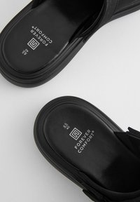 Mustat sandaalit, joissa on sileä nahkapinta, pehmustettu pohja ja tyylikäs muotoilu. Hänellä on logo ja kokomerkinnät jalkapohjassa.