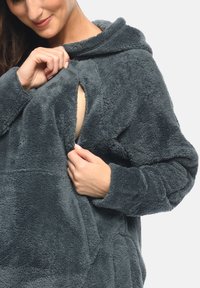 Grauer, samtiger Kapuzenpullover mit einem Frontverschluss. Weicher, strukturierter Stoff und lockere Passform mit umgelegten Ärmeln. Teilweise sichtbarer Reißverschluss.