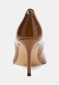 Zapato de tacón alto de charol marrón con punta afilada, tacón fino de aguja y un detalle plateado en la parte trasera. Textura lisa y brillante.