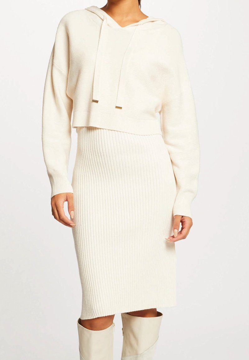 Hoodie court de couleur crème avec texture côtelée, associé à une jupe côtelée longueur genou. Les deux pièces ont une finition en tissu doux.