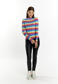 Maglione a righe multicolore con maniche lunghe, coste testurizzate e un collo viola, abbinato a pantaloni neri lucidi e sneakers pastello.