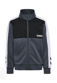 Kurtka sportowa w ciemnym granacie z wysokim kołnierzem, kontrastującą czarną górną częścią, białymi rękawami oraz czarnymi akcentami w kształcie szewrona. Pełny zamek błyskawiczny z przodu.