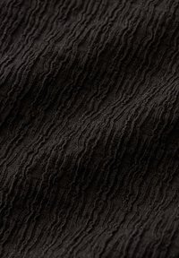 Black fabric with raised wavy textured lines creating a rippled pattern and varying light and shadow across the surface.