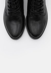 Svarta läderankelboots med slät textur, rundade tår och snören som går upp till ankeln. Har en sydd design längs kanterna.