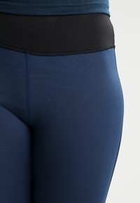 Leggings blu navy con una cintura alta nera, texture liscia e cuciture a contrasto lungo le giunzioni.