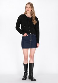 Zwarte gebreide trui met zilveren stippen en een strikdetail, gecombineerd met een donkerdenim minirok en hoge zwarte laarzen met gespen.