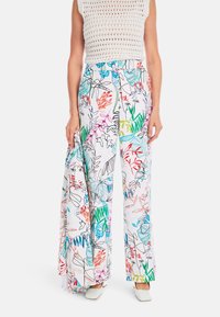 Bunte, blütenmusterierte, weit geschnittene Hosen aus leichtem Stoff mit einem weißen Grundton und lebhaften Grüntönen, Rottönen und Blautönen.