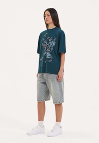 Overdimensioneret teal t-shirt med grafisk print af en zebra og en slange; parret med lyseblå denimshorts og hvide sneakers.