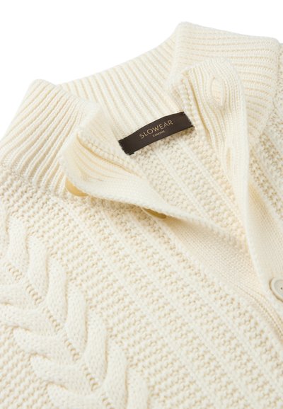 Crèmekleurige gebreide cardigan met een sjaalkraag, textuurpatronen en twee knopen. Etiket leest "SLOWEAR ZANONI."