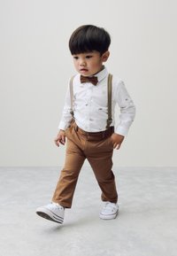 White shirt with light embroidery, brown bow tie, tan trousers, beige suspenders, and white sneakers. Simple and classic design.