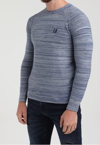 Jersey de punto de manga larga en azul con rayas horizontales texturizadas. Presenta un cuello redondo y un pequeño logo en el pecho.